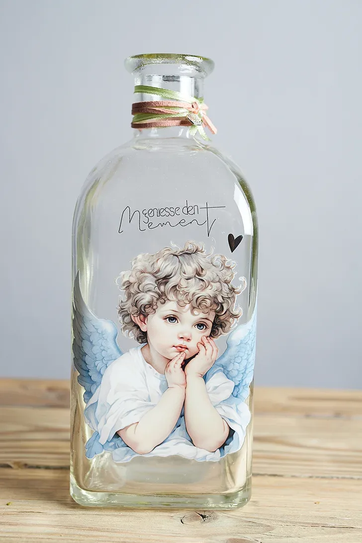 Glasflasche mit Engelaufdruck und Herzform auf Holzuntergrund.